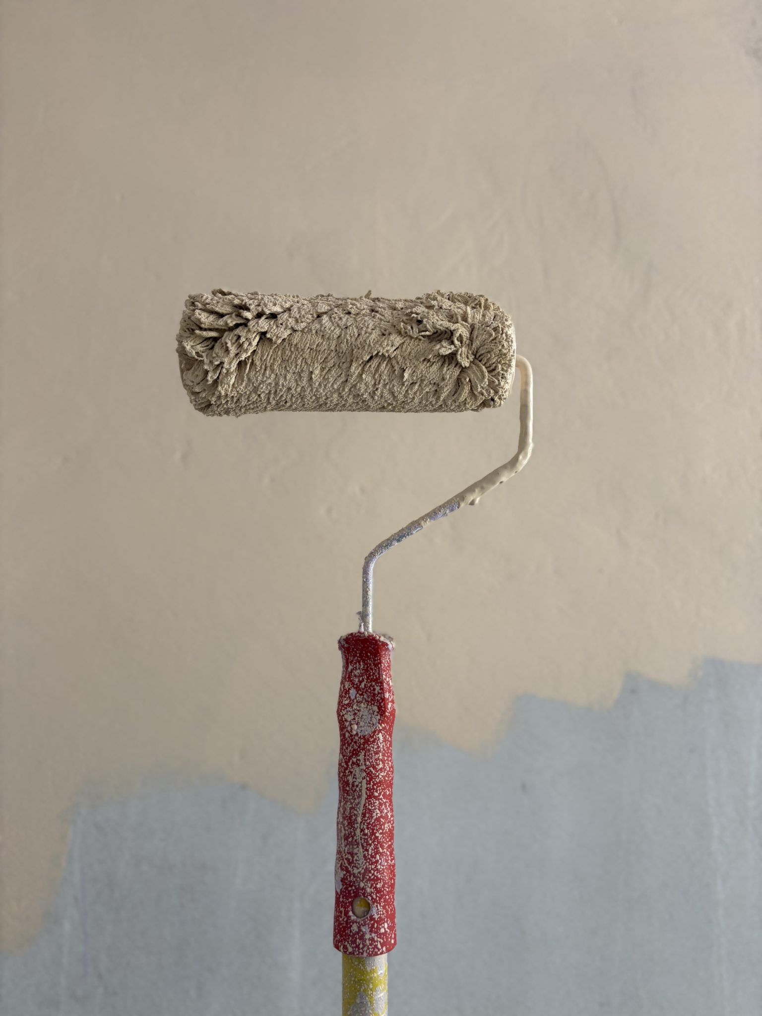 A paint roller held against a wall that is half painted